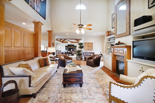 living room featuring hardwood / wood-style flooring, ceiling fan, a fireplace, built in shelves, and ornate columns