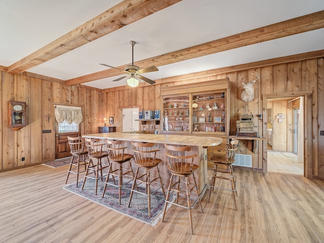 kitchen with light wood-type flooring, beamed ceiling, a breakfast bar area, wood walls, and ceiling fan