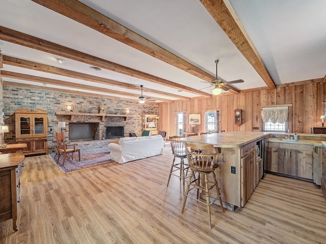 kitchen with light wood-type flooring, a fireplace, ceiling fan, and a breakfast bar