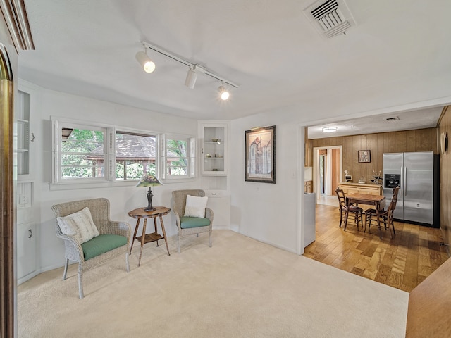 sitting room with rail lighting, light hardwood / wood-style floors, and wooden walls