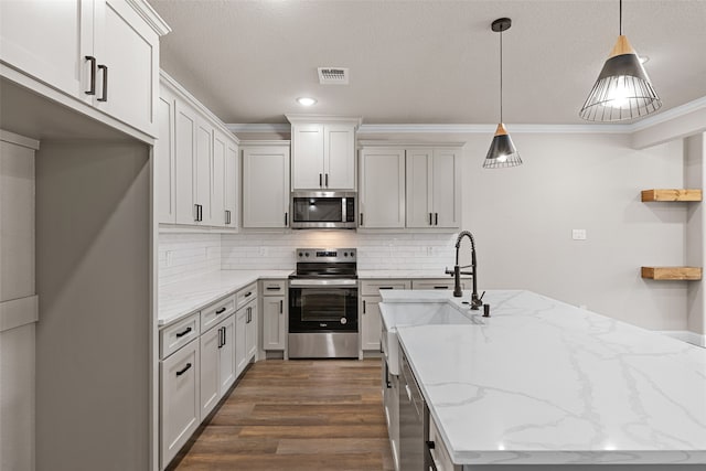 kitchen featuring dark hardwood / wood-style flooring, appliances with stainless steel finishes, light stone counters, decorative light fixtures, and crown molding