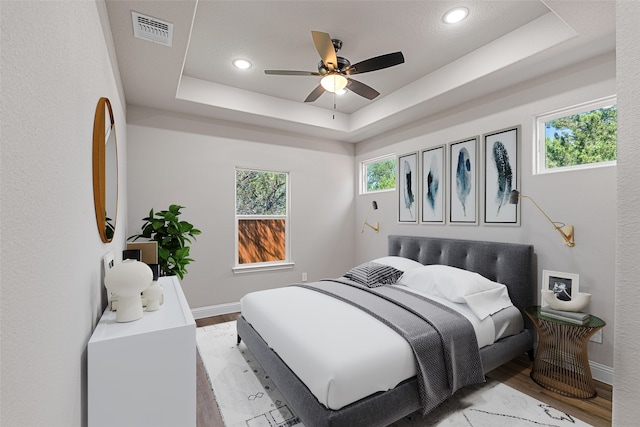 bedroom featuring ceiling fan, a raised ceiling, and light hardwood / wood-style floors