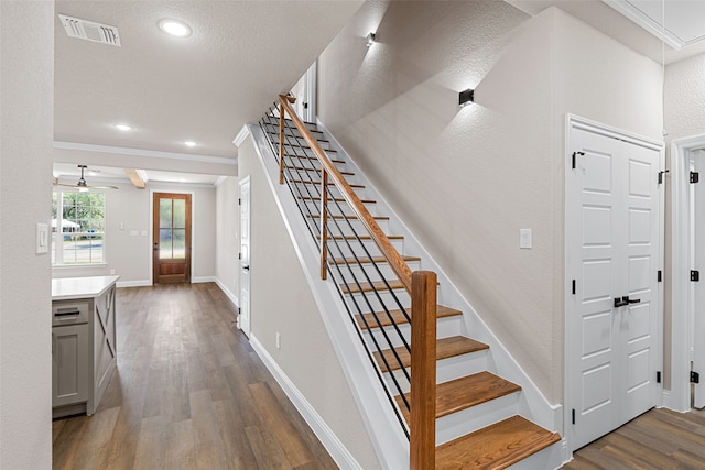 stairway featuring ceiling fan, wood-type flooring, ornamental molding, and a textured ceiling