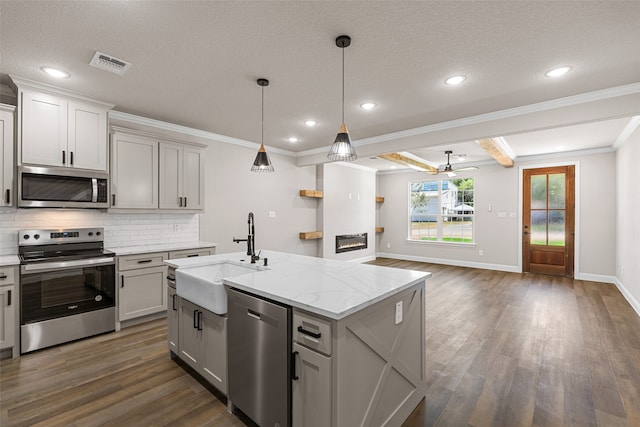 kitchen featuring dark wood-type flooring, a kitchen island with sink, appliances with stainless steel finishes, sink, and crown molding