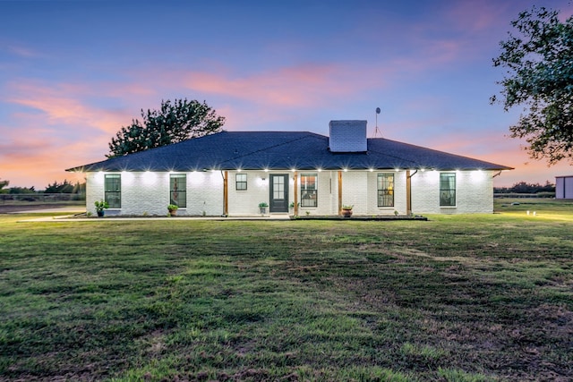 back of property featuring a chimney, a lawn, and brick siding