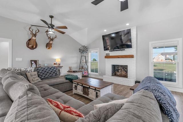 living room with brick wall, lofted ceiling, wood-type flooring, ceiling fan, and a brick fireplace