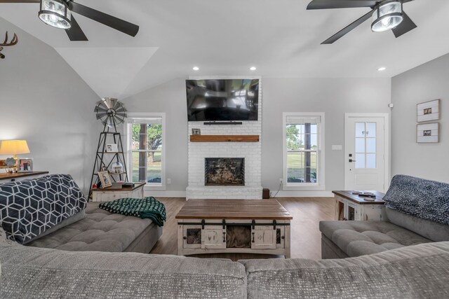 living room with brick wall, lofted ceiling, wood-type flooring, ceiling fan, and a brick fireplace