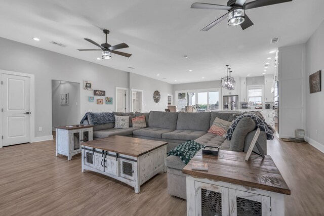 living room featuring light wood-type flooring and ceiling fan with notable chandelier