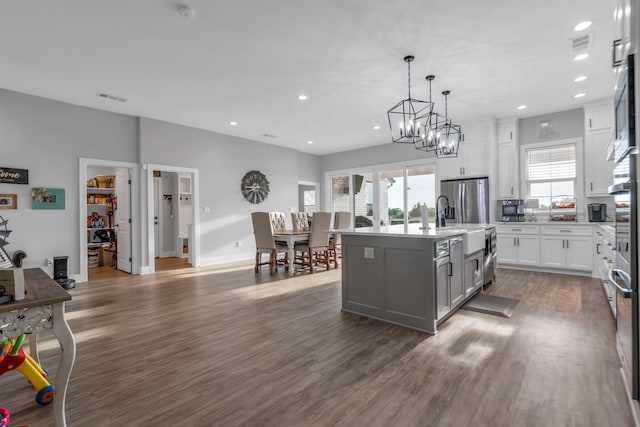 kitchen featuring decorative light fixtures, hardwood / wood-style flooring, an island with sink, stainless steel refrigerator with ice dispenser, and white cabinets