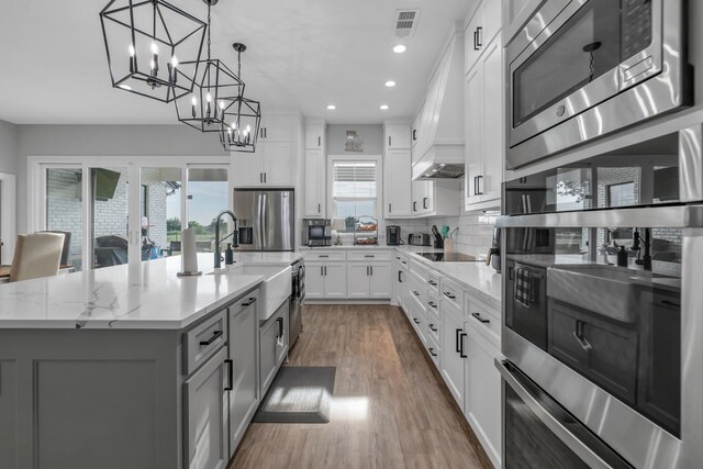 kitchen featuring white cabinets, custom exhaust hood, an island with sink, and stainless steel appliances