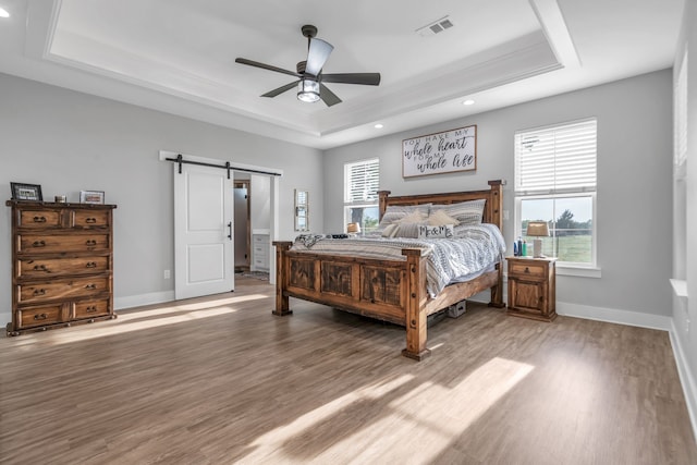 bedroom with wood finished floors, a raised ceiling, visible vents, and a barn door