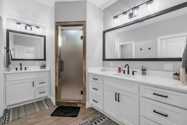 full bathroom with a shower stall, two vanities, a sink, and wood finished floors