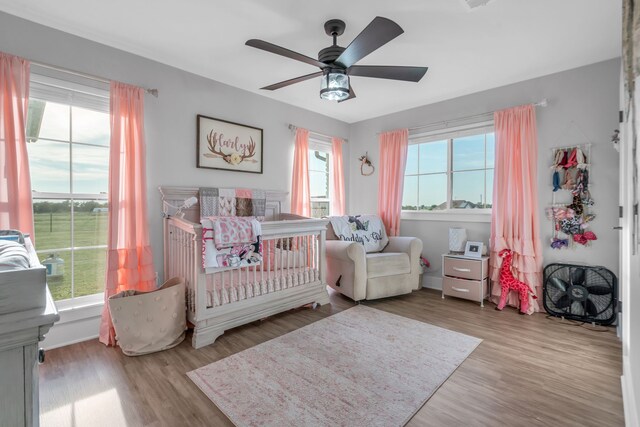 bedroom featuring ceiling fan, a crib, hardwood / wood-style floors, and multiple windows