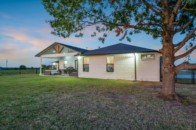 back house at dusk with an outdoor hangout area, a patio area, and a yard