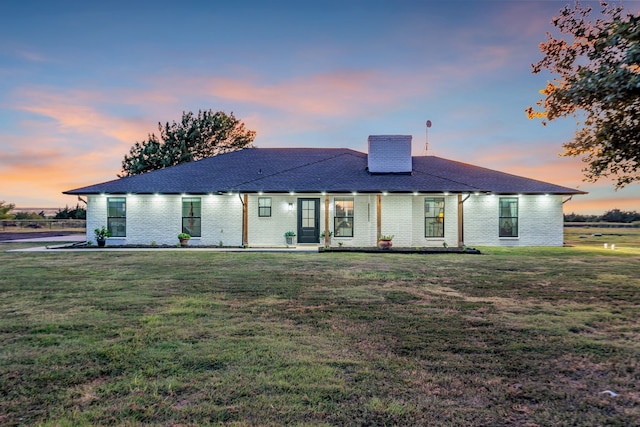 view of front of house featuring brick siding, a chimney, a front lawn, and roof with shingles