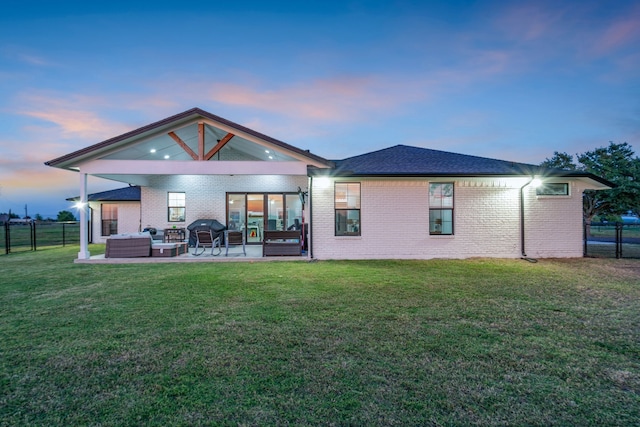 back house at dusk with a patio, a yard, and an outdoor living space