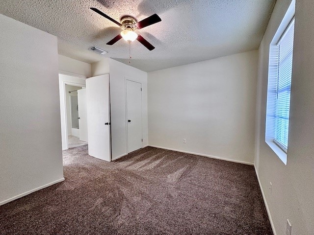 unfurnished bedroom with a textured ceiling, dark carpet, and ceiling fan