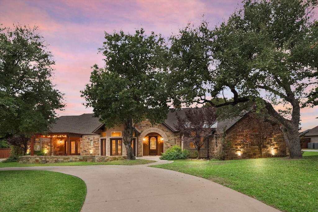 view of front of home featuring driveway, a lawn, and stone siding