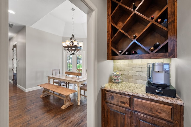 bar with decorative backsplash, a chandelier, dark brown cabinets, dark wood-type flooring, and hanging light fixtures