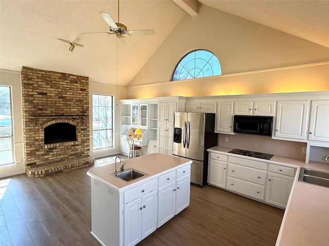 kitchen featuring a kitchen island with sink, a fireplace, a sink, black appliances, and dark wood finished floors