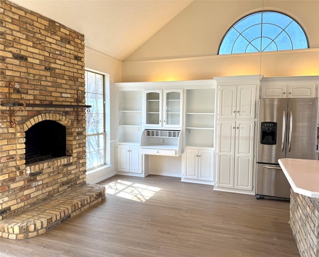 unfurnished living room featuring lofted ceiling, a brick fireplace, a textured ceiling, and wood finished floors