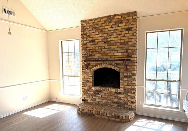 unfurnished living room with vaulted ceiling, a textured ceiling, wood finished floors, and visible vents