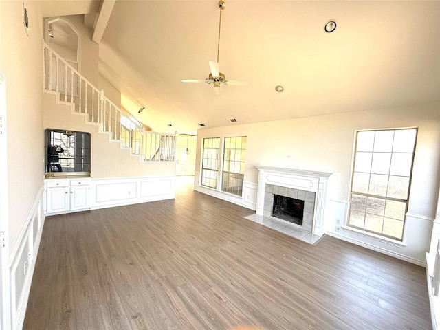 unfurnished living room featuring ceiling fan, high vaulted ceiling, a tile fireplace, wood finished floors, and stairs