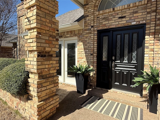 view of exterior entry with a shingled roof, a chimney, and brick siding