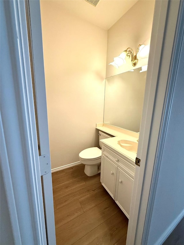 half bath with toilet, baseboards, wood finished floors, and vanity