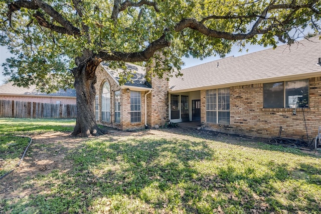 rear view of house featuring a yard, brick siding, and fence