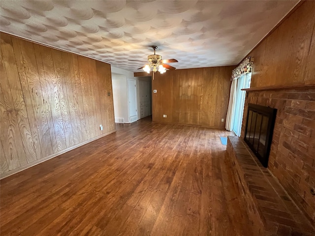 unfurnished living room featuring hardwood / wood-style floors, ceiling fan, wood walls, and a fireplace