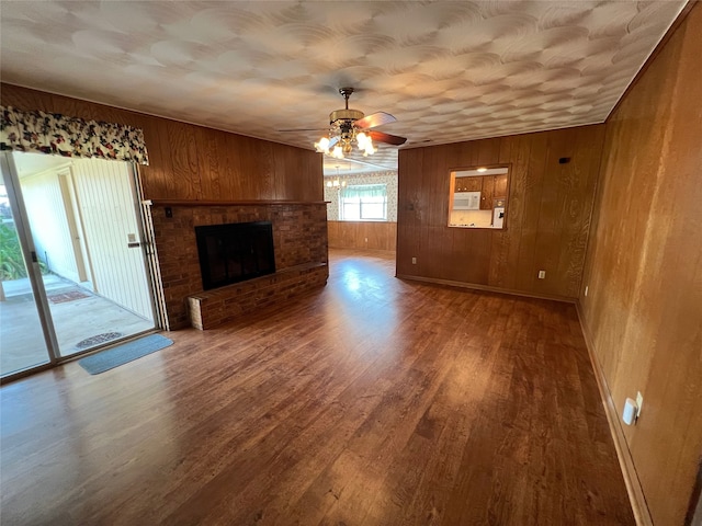 unfurnished living room with ceiling fan, wooden walls, hardwood / wood-style flooring, and a brick fireplace