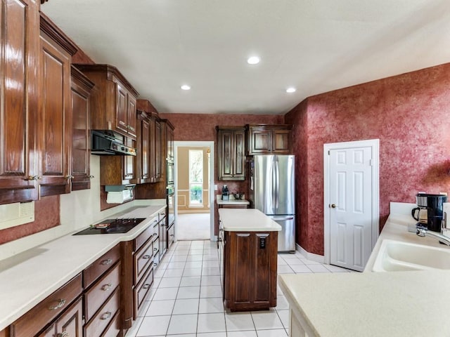 kitchen with a kitchen island, freestanding refrigerator, black electric stovetop, under cabinet range hood, and a sink