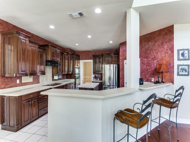 kitchen featuring visible vents, freestanding refrigerator, black electric cooktop, light countertops, and under cabinet range hood