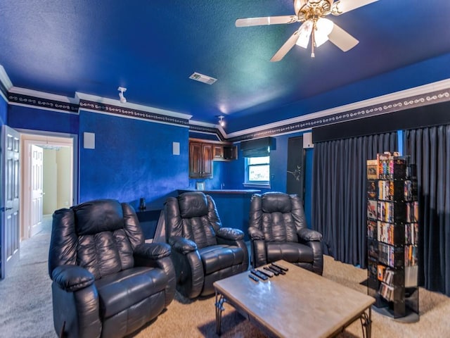 carpeted home theater room with ornamental molding, visible vents, ceiling fan, and a textured ceiling