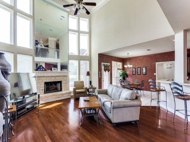 living area featuring ceiling fan with notable chandelier, a healthy amount of sunlight, a stone fireplace, and wood finished floors