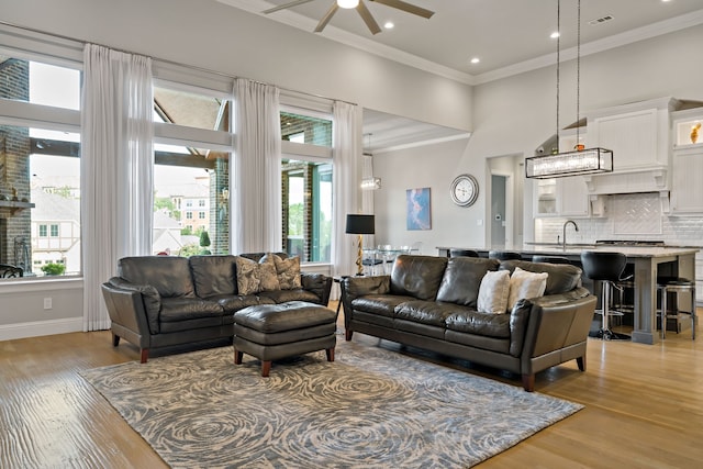 living room featuring light hardwood / wood-style flooring, a towering ceiling, ceiling fan, ornamental molding, and sink