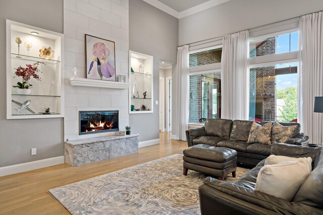 living room with a tile fireplace, a high ceiling, crown molding, and light hardwood / wood-style floors