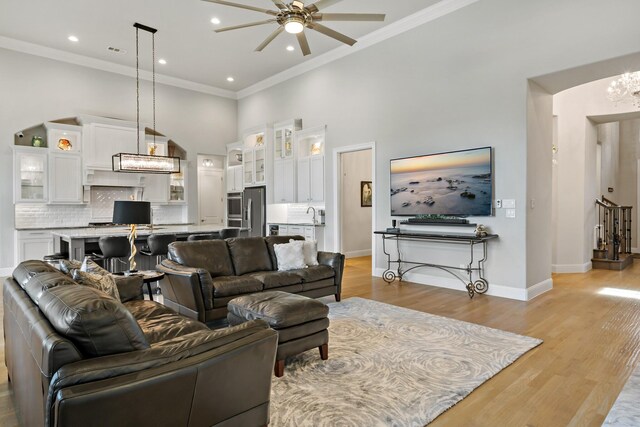 living room featuring light hardwood / wood-style flooring, a high ceiling, ornamental molding, sink, and ceiling fan with notable chandelier