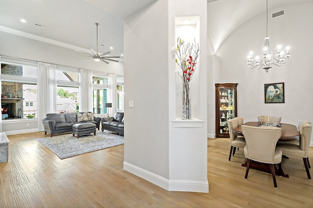 dining room featuring a brick fireplace, light wood-type flooring, high vaulted ceiling, and ceiling fan with notable chandelier