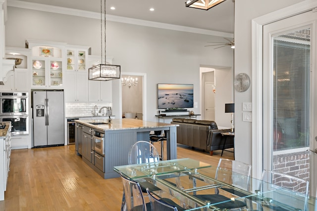 kitchen featuring a center island with sink, light wood-type flooring, white cabinetry, decorative light fixtures, and stainless steel appliances