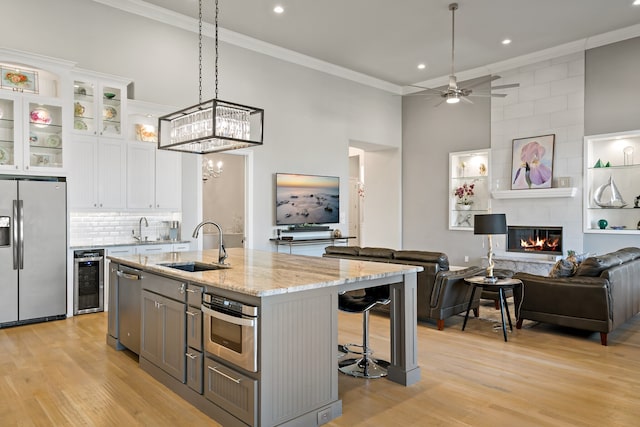 kitchen with stainless steel appliances, a kitchen island with sink, beverage cooler, a tile fireplace, and white cabinetry