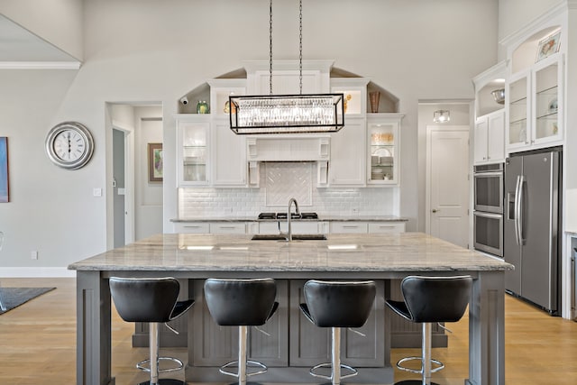 kitchen with stainless steel refrigerator with ice dispenser, a breakfast bar, a notable chandelier, white cabinetry, and an island with sink