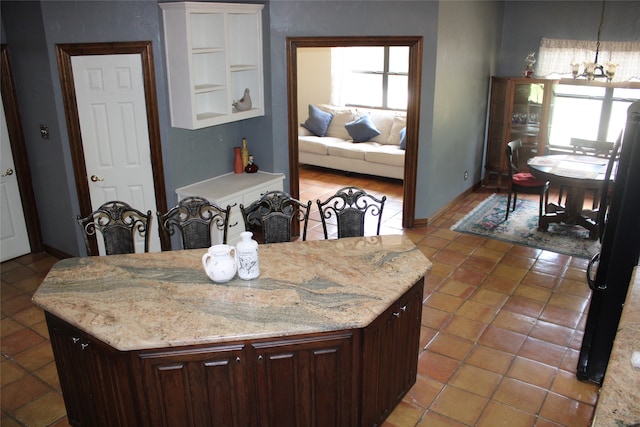 kitchen with light tile patterned flooring, an inviting chandelier, light stone counters, and dark brown cabinetry