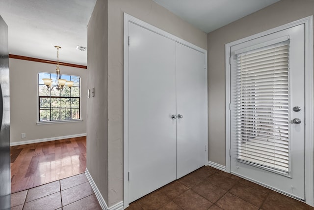 tiled entryway with baseboards, visible vents, a chandelier, and ornamental molding