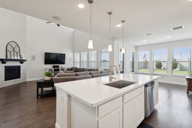 kitchen featuring sink, white cabinets, dishwasher, a large fireplace, and a kitchen island with sink