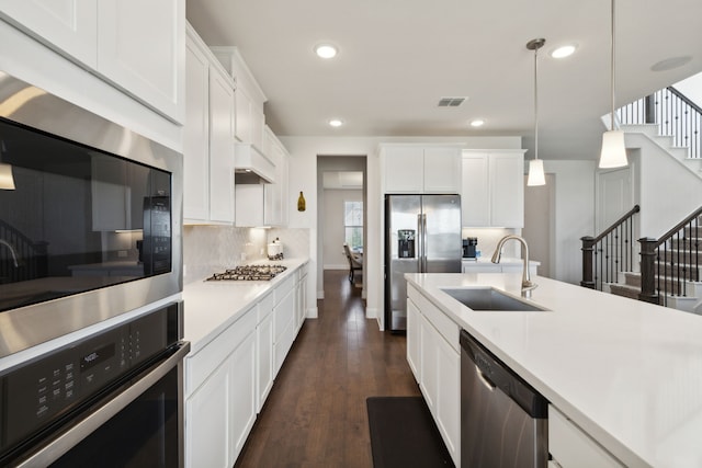 kitchen featuring appliances with stainless steel finishes, white cabinets, decorative light fixtures, and sink