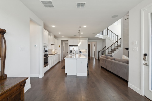 kitchen with decorative light fixtures, white cabinets, a center island with sink, and a kitchen breakfast bar