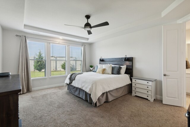 bedroom with ceiling fan, light colored carpet, and a tray ceiling