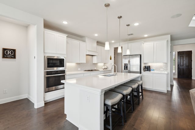 kitchen with appliances with stainless steel finishes, an island with sink, pendant lighting, white cabinets, and sink